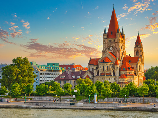 Das Bild einer Stadt in Österreich mit einer Kirche und einem Fluss im Vordergrund.